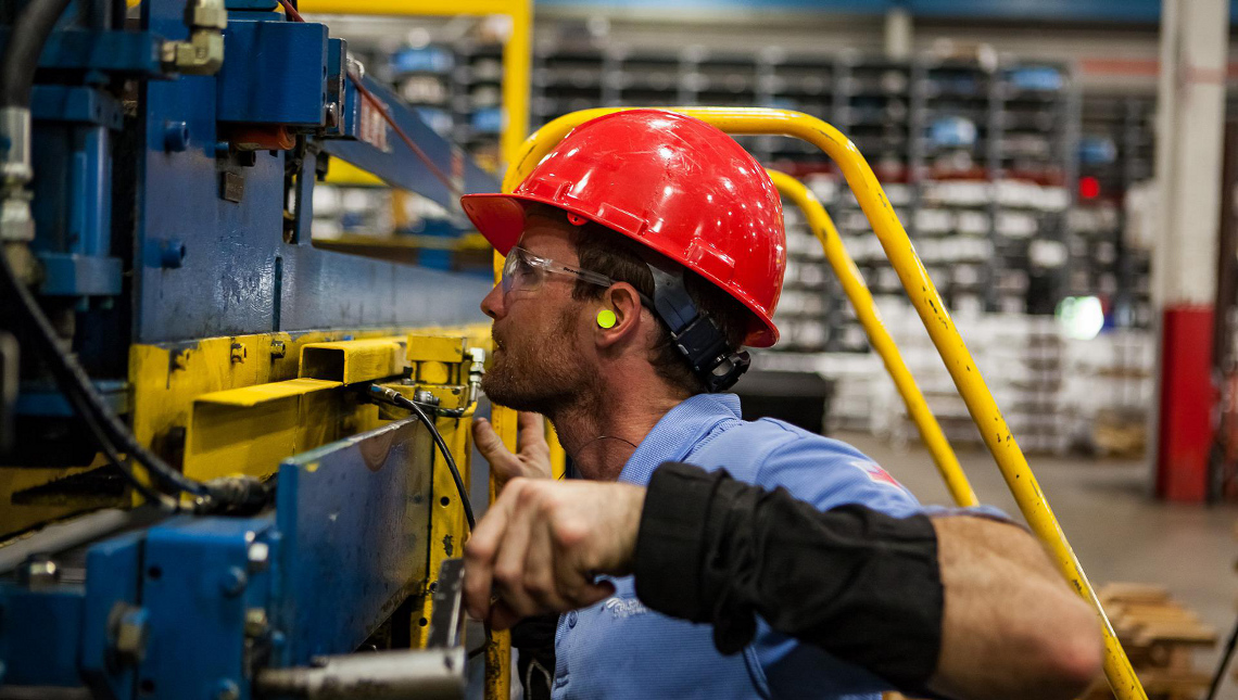 Arbeiter mit Schutzhelm und Schutzbrille betätigt eine große Industriemaschine.