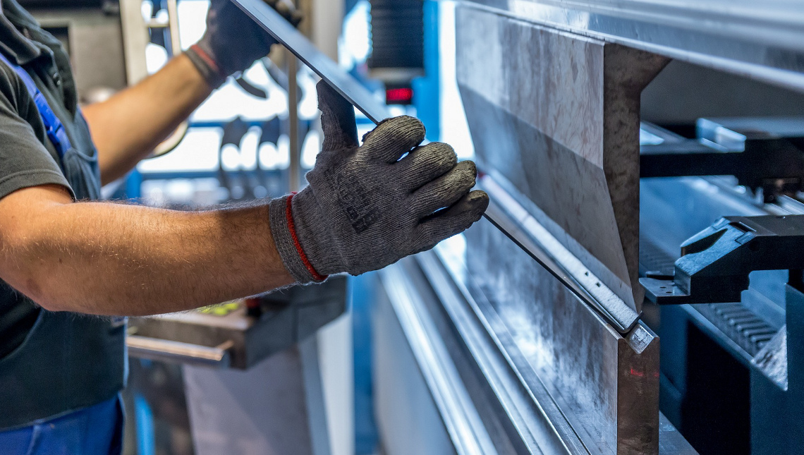 Arbeiter mit Schutzhandschuhen bearbeitet Metallplatte maschinell